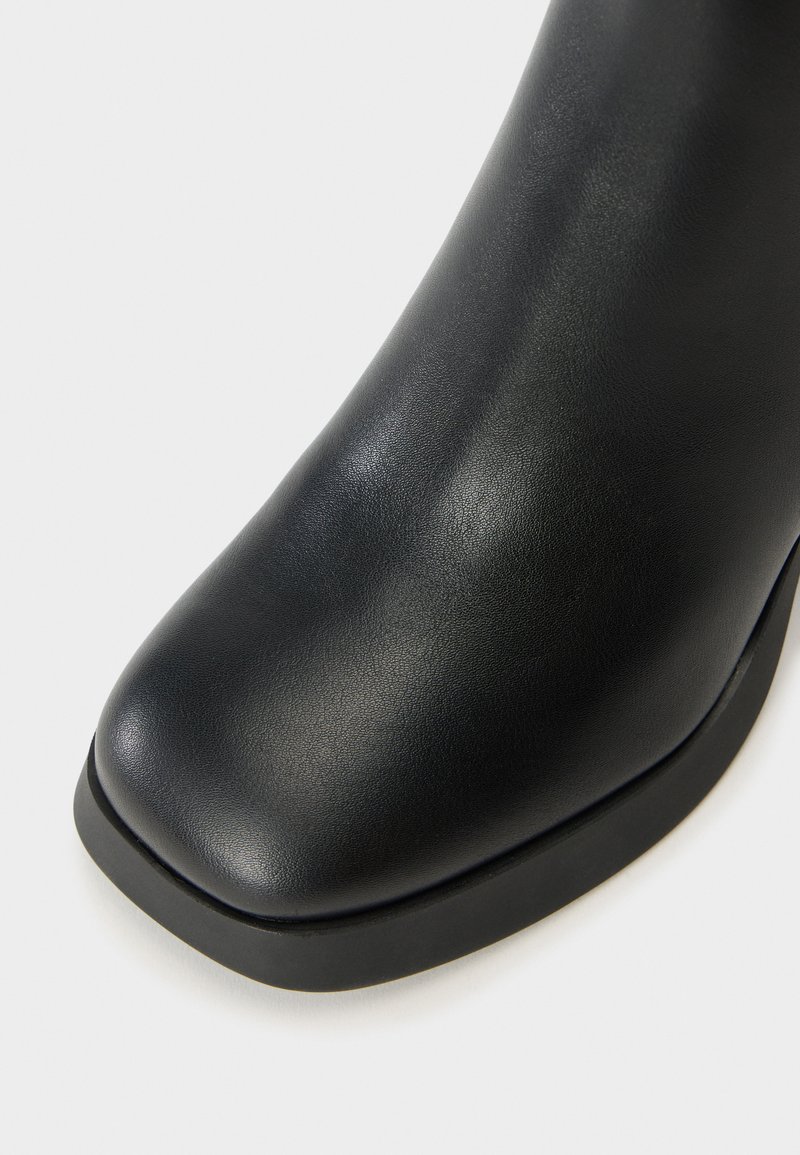 Zwarte leren enkelboot met een ronde neus, een gladde textuur en een licht verhoogde rubberen zool. Minimalistisch ontwerp zonder zichtbare hardware.