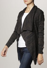 Lång mörk tröja med draperad front, textiler i strukturerad kvalitet med mörka ränder, öppna ärmar och små accentdetaljer på muddarna.