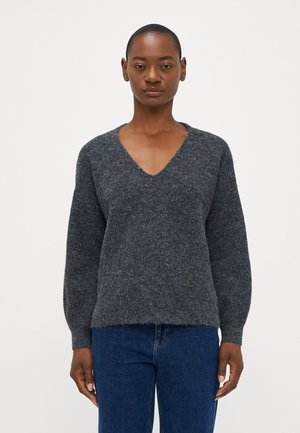 Pull gris charbon avec un col en V, texture douce et manches longues. Tissu en maille avec une coupe légèrement ample, associé à un jeans bleu.