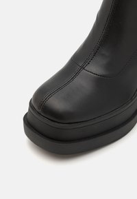 Bottine en cuir noir avec un bout rond et une semelle plateforme. Présente des surpiqûres décoratives le long de la tige et une texture lisse.