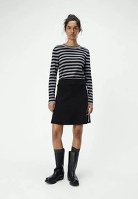 Haut à rayures à manches longues en gris et noir, associé à une jupe noire. Le modèle porte des bottes noires jusqu'au genou avec des accents verts côtelés.