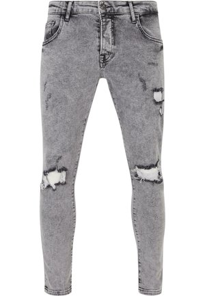 Jeans en denim gris avec une coupe slim, présentant des zones usées et des déchirures au niveau des genoux. Design à cinq poches avec une fermeture à bouton classique.