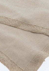 Miękka beżowa tkanina z luźno tkanym metalicznym złotym zdobieniem na brzegach, tworzącym teksturowaną ramkę.