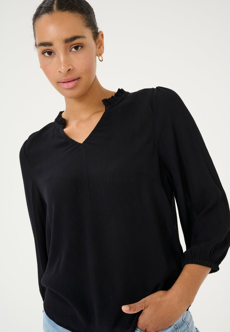 Zwarte blouse met een V-hals en gerimpelde halslijn. Lange mouwen met gekruiste manchetten. Lichtgewicht stof met een gestructureerde afwerking.