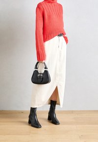 Schwarze Lederhandtasche mit silberner Hardware, kombiniert mit einem korallenfarbenen Strickpullover und einem cremefarbenen Rock mit seitlicher Schlitze, ergänzt durch schwarze Ankle Boots.