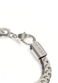 Bracciale in argento con maglie grandi, dotato di una chiusura a barra lucidata. Il logo "GUESS" è inciso sulla chiusura. Texture liscia in tutto il bracciale.