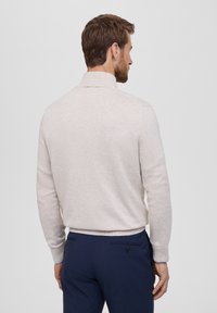 Maglione beige con colletto, polsini e orlo a coste. Abbinato a pantaloni blu navy, che mostrano una superficie sia liscia che strutturata. Design minimalista.