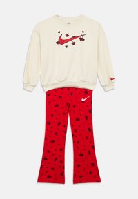 Φούτερ εκρού με κόκκινο logo Nike swoosh και γραφικά με κερασάκια σε σχήμα καρδιάς, συνδυασμένο με κόκκινο παντελόνι που έχει μαύρα κεράσια και σχέδια καρδιάς καθώς και λευκό λογότυπο Nike.