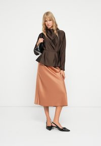 Bruine satijnen blouse met een peplum taille, gecombineerd met een lichtbruine satijnen rok. Zwarte slingback schoenen met een strikdetail.
