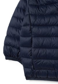 Chaqueta de plumas azul marino con un patrón acolchado, que presenta una tela suave y lisa, y un dobladillo acanalado. Incluye un pequeño detalle de bolsillo con cremallera.