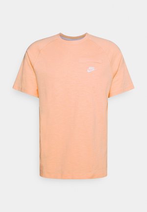 Licht perzikkleurig Nike T-shirt met korte mouwen en ronde hals, met een klein wit logo op de linkerborst, effen ontwerp tegen een effen achtergrond.