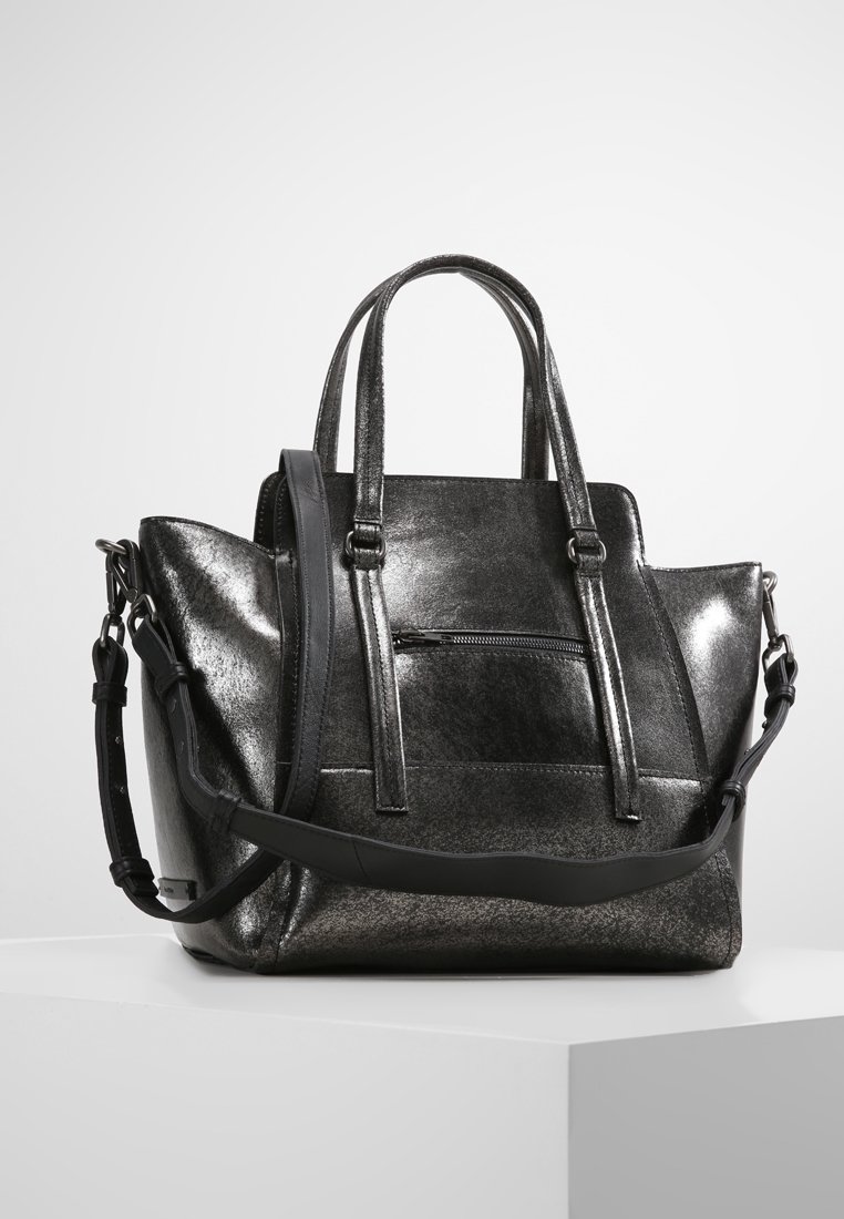 Sac à main en cuir noir brillant avec doubles poignées, poche zippée à l'avant et bandoulière ajustable sur une surface blanche.