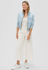 Hellblaues Jeans-Shortjackett, weißes geripptes Top, weiße weiter geschnittene Hose mit fransigem Saum und weiße Sneakers. Einfache, legere Outfit.