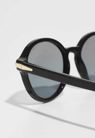 Black round sunglasses with gradient lenses, smooth plastic frame, and gold accents on the hinges. Sleek design with a minimalistic look.
