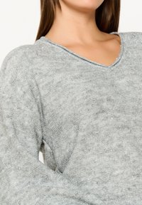 Hellgrauer Strickpullover mit V-Ausschnitt, dezent schimmerndem Effekt und weichem, strukturiertem Stoff. Lockerer Schnitt mit langen Ärmeln.