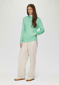 Mintgrüner Langarm-Hoodie mit abgerundetem Saum und Kängurutasche; kombiniert mit beigen, weiten Hosen und hellen Sneakers.