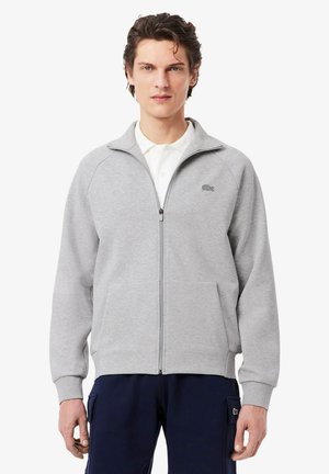 Grijze rits-sweater gemaakt van een katoenmix, met een hoge kraag, ribgebreide manchetten en een logo op de linkerkant van de borst. Gecombineerd met marineblauwe broek.