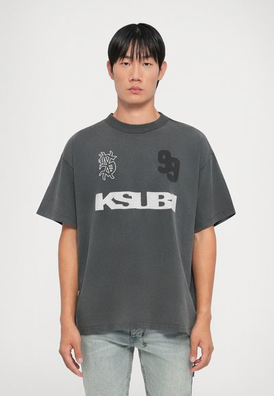 Grijze oversized t-shirt met korte mouwen, voorzien van een witte "KSUBI" logo en verschillende zwarte grafische prints voor extra details.