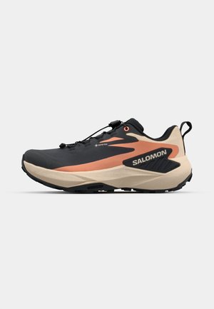 Black and beige trail running shoe with a textured upper, Gore-Tex branding, and orange accents, featuring a lugged outsole for traction.