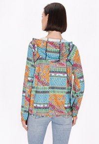 Giacca con cappuccio dal design patchwork in colori vivaci, caratterizzata da motivi floreali e geometrici. Tessuto leggero con maniche lunghe.