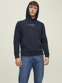 Hanorac navy cu șnururi, buzunar kangaroo și logo pe față. Purtați cu blugi albaștri deschiși, evidențiind o croială relaxată și o textură moale.