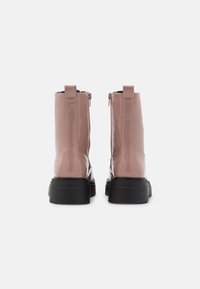 Bottines en cuir verni rose avec une semelle noire épaisse et des zips sur le côté. Équipées d'une languette à l'arrière pour un enfilage facile.