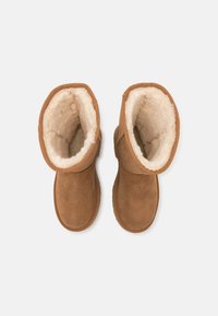 Bottes cheville en daim marron avec une doublure en fourrure douce de couleur crème, bout rond et accents cousus en haut. Semelle plate.