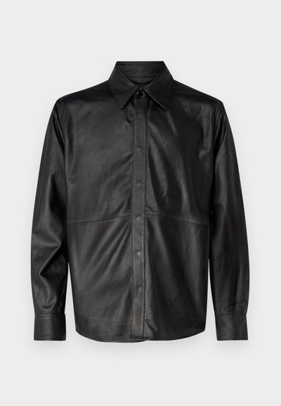 Must musta särgijakk, millel on terav krae, ees nööbid, pikad varrukad ja nähtavad õmblusdetailid. Sile tekstuur.