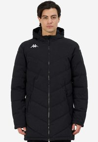 Giacca imbottita nera con cappuccio, caratterizzata da un motivo trapuntato a zigzag, chiusura con zip e logo sul petto. Due tasche laterali con zip.