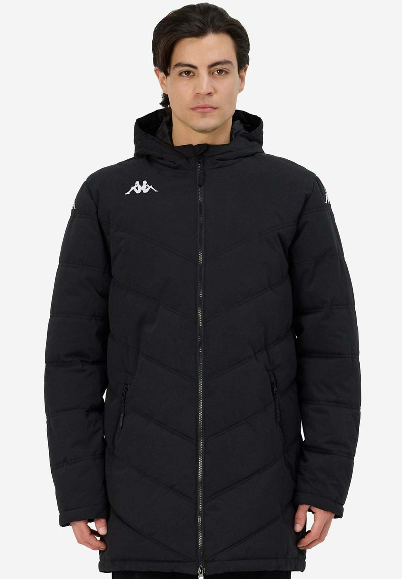 Giacca imbottita nera con cappuccio, caratterizzata da un motivo trapuntato a zigzag, chiusura con zip e logo sul petto. Due tasche laterali con zip.