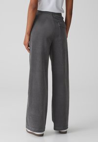 Pantalon large en velours côtelé gris avec un tissu texturé, une taille élastique et un détail de poche arrière. Vue de dos et de l'ourlet.