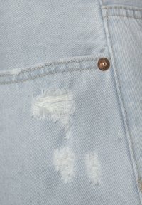 Lichtblauwe denimstof met gescheurde details, koperen knoopaccenten en een gestructureerd weefpatroon.