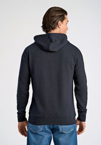 Felpa con cappuccio di un blu navy scuro in tessuto texturizzato, con cappuccio regolabile e polsini a coste, abbinata a jeans blu chiaro.