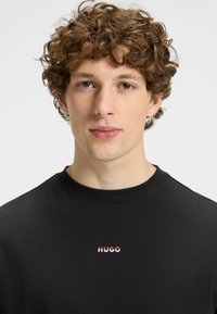 Sweatshirt en coton noir avec le logo "HUGO" en rouge et blanc sur la poitrine. Encolure ronde simple et texture douce.