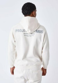 Witte hoodie met een groot bedrukte logo op de achterkant, gemaakt van zachte stof met een relaxte pasvorm en een verstelbare trekkoordcapuchon.