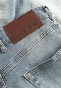 Lichtblauwe denim jeans met een bruine leren label met de tekst "GABBA". Zichtbare stiksels en zakdetails verbeteren het ontwerp.