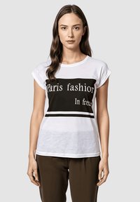 Camiseta blanca de manga corta con un gráfico negro que presenta "Moda de París" y "En libertad" en texto blanco en negrita. Tejido suave, corte relajado.