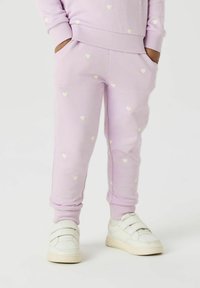 Lilla sweatpants med små, reflekterende hjerte mønstre, elastiske manchetter og sidelommer. Parret med hvide velcro sneakers.
