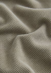 Tissu beige en maille gaufrée avec un motif de grille texturé et des plis doux créant des plis ombragés.