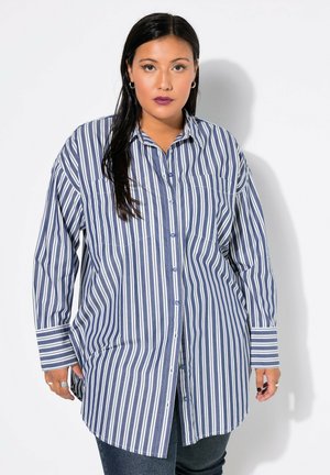 Camicia a maniche lunghe a righe verticali blu e bianche con tasche sul petto e orlo arrotondato. Il tessuto sembra leggero e con una texture.