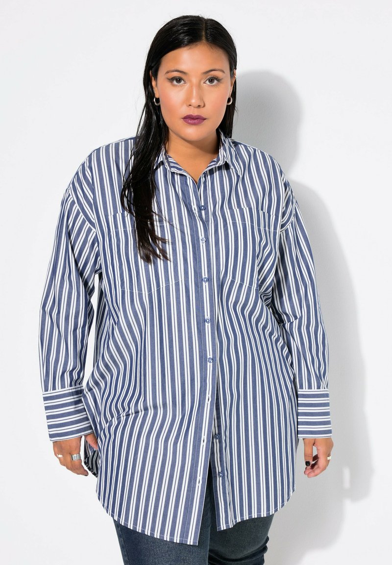 Camicia a maniche lunghe a righe verticali blu e bianche con tasche sul petto e orlo arrotondato. Il tessuto sembra leggero e con una texture.