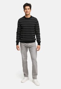Stribet sweater i sort og hvid med rund hals, parret med lys grå lige ben jeans og hvide sneakers. Enkel, afslappet design.