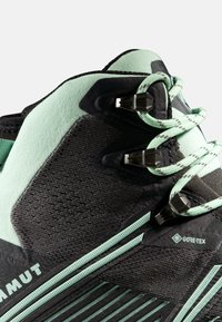 Scarpe da hiking nere e verde menta con tomaia testurizzata, accenti a strisce e marchio GORE-TEX. Comprendono ganci neri per lacci e materiali resistenti.
