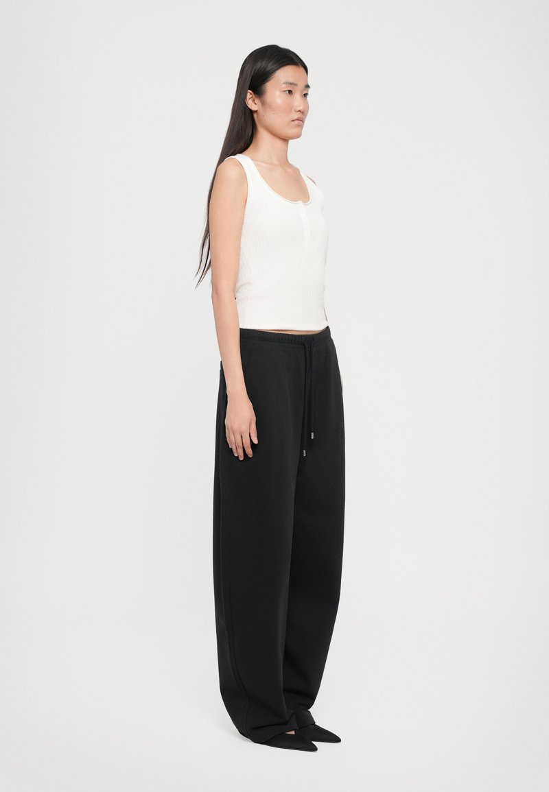 Débardeur blanc à côtes avec encolure henley, associé à un pantalon de jogging noir ample avec taille élastique et cordon de serrage.