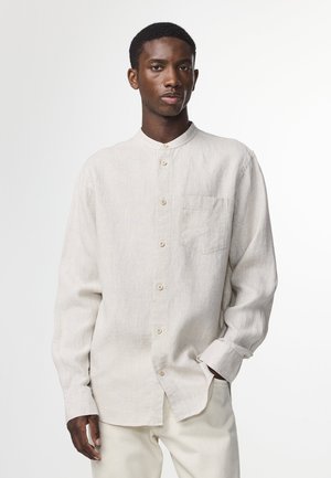 Lys beige langærmet skjorte lavet af linen. Har en rund krave, frontlomme og knaplukning. Tekstureret stof med et subtilt mønster.