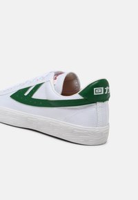 White sneakers with green leather accents, featuring a smooth texture, lace-up design, and a patterned rubber sole. Branding on heel.