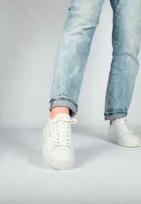 Weiße Ledersneaker mit strukturiertem Finish und flachen Schnürsenkeln, kombiniert mit hellblauen, abgetragenen Jeans mit hochgekrempeltem Saum.