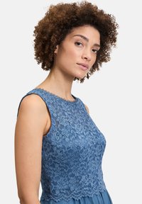 Blauwe kant jurk met een nauwsluitende lijfje met bloemenpatronen en een scalloped halslijn, dieovergaat in een gladde, geplooide rok.