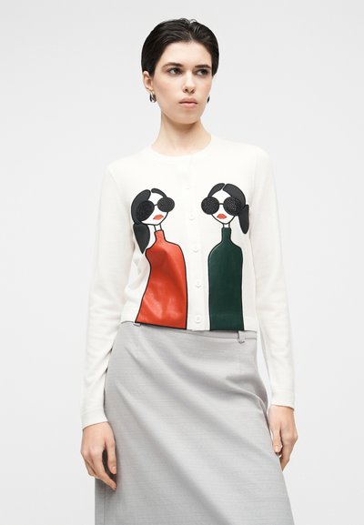 Bela jopa z dvema stiliziranima figurama v rdeči in zeleni barvi, z rjavimi sončnimi očali in podrobnimi obraznimi potezami, spredaj na gumbe.
