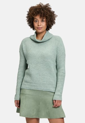 Lichtgroene trui met een col, textuurgebreid en lange mouwen, gecombineerd met een bijpassende leren minirok.